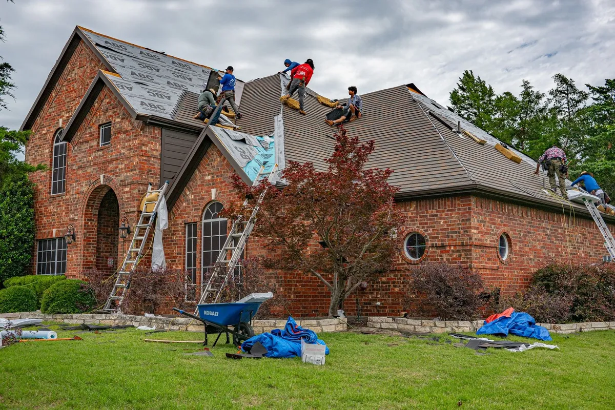Roofers installing shingles on a brick home, illustrating the work of a roofing company.